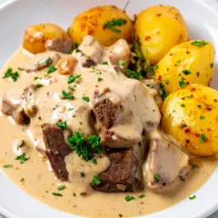 Schab w kremowym sosie z grzybami i pieczonymi ziemniakami, udekorowany natką pietruszki.