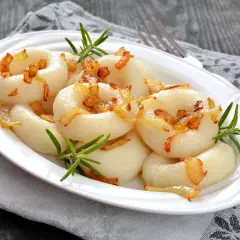 Kluski śląskie z podsmażoną cebulką i rozmarynem na białym talerzu.