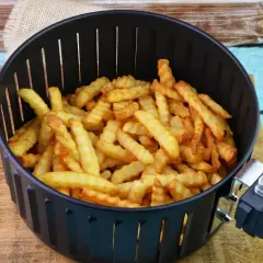 Koszyk frytkownicy wypełniony złocistymi, pofalowanymi frytkami.