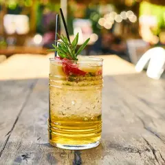 Szklanka orzeźwiającego drinka z lodem, owocami i gałązką rozmarynu na drewnianym stole.