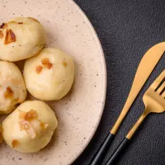 Kluski śląskie z cebulką na talerzu obok złotych sztućców.