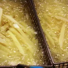 Frytki smażące się w gorącym oleju w metalowych koszach.