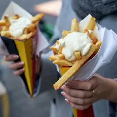 Dwie porcje frytek w papierowych rożkach, polane majonezem.
