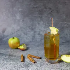 Szklanka z drinkiem, jabłka, laska cynamonu na szarym tle.