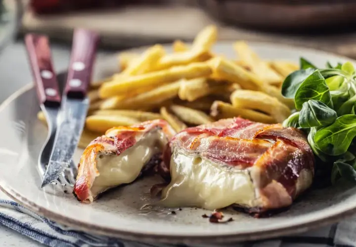 Ser camembert zawinięty w bekon, podany z frytkami i sałatką.