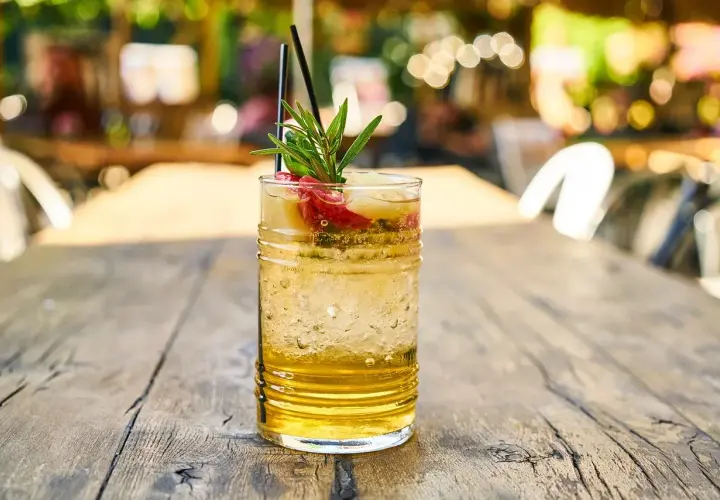 Szklanka orzeźwiającego drinka z lodem, owocami i gałązką rozmarynu na drewnianym stole.