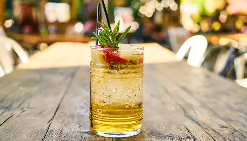 Szklanka orzeźwiającego drinka z lodem, owocami i gałązką rozmarynu na drewnianym stole.