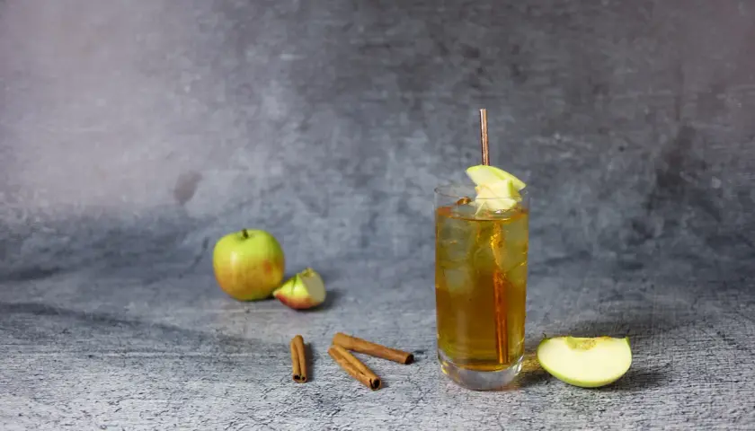 Szklanka z drinkiem, jabłka, laska cynamonu na szarym tle.