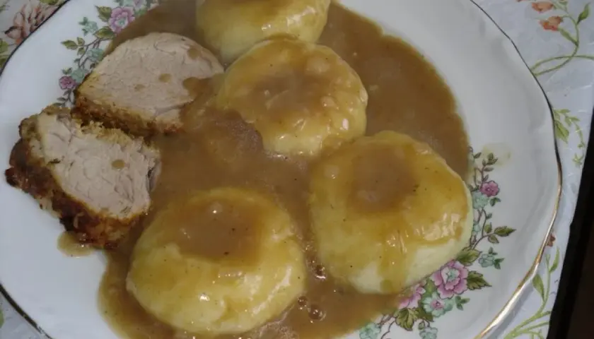 Kluseczki śląskie z mięsem i sosem na talerzu z kwiatowym wzorem.